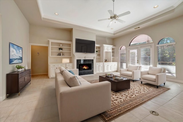 living room featuring a fireplace, light tile patterned floors, a tray ceiling, and ceiling fan