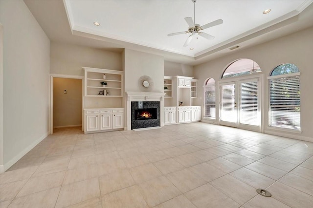 unfurnished living room featuring ceiling fan, a raised ceiling, built in features, a high end fireplace, and light tile patterned floors