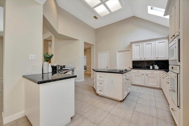 kitchen featuring backsplash, white cabinets, sink, a skylight, and kitchen peninsula