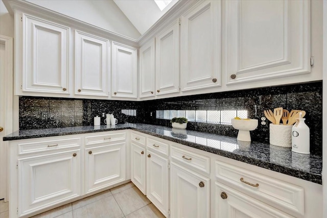 kitchen featuring white cabinetry, vaulted ceiling, dark stone counters, and light tile patterned flooring