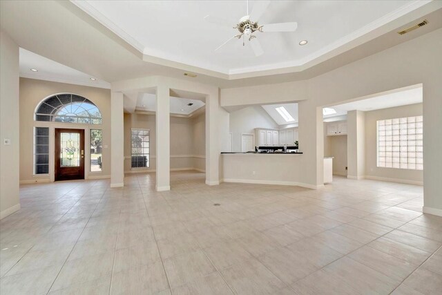 unfurnished living room featuring ceiling fan, a raised ceiling, ornamental molding, and light tile patterned floors