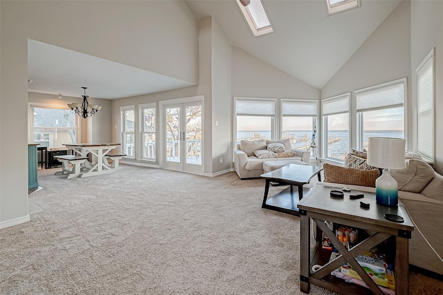 living room with a skylight, a high ceiling, a water view, a notable chandelier, and light carpet