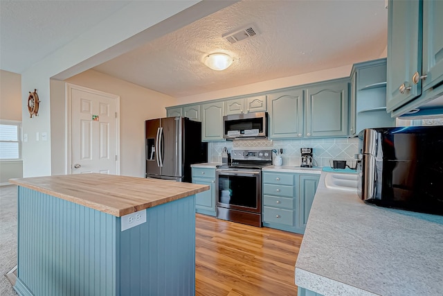 kitchen with butcher block countertops, a center island, appliances with stainless steel finishes, light hardwood / wood-style floors, and backsplash