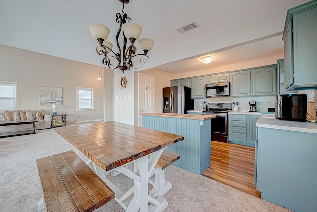 kitchen featuring decorative light fixtures, light countertops, visible vents, appliances with stainless steel finishes, and open floor plan