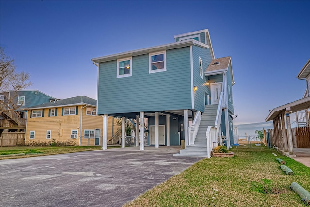 coastal inspired home featuring driveway, stairs, a front lawn, and a carport