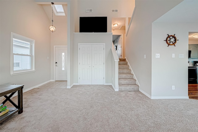 entryway with light carpet, a skylight, baseboards, stairs, and high vaulted ceiling