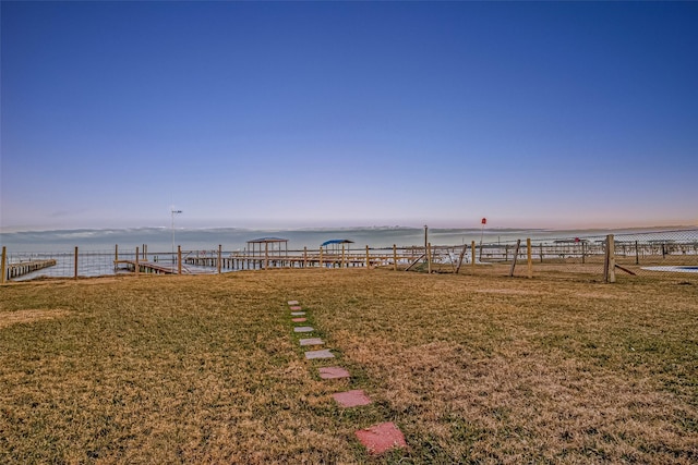 yard at dusk featuring a water view and fence