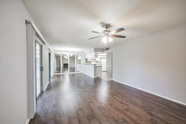 unfurnished living room with ceiling fan with notable chandelier, dark hardwood / wood-style floors, and a textured ceiling