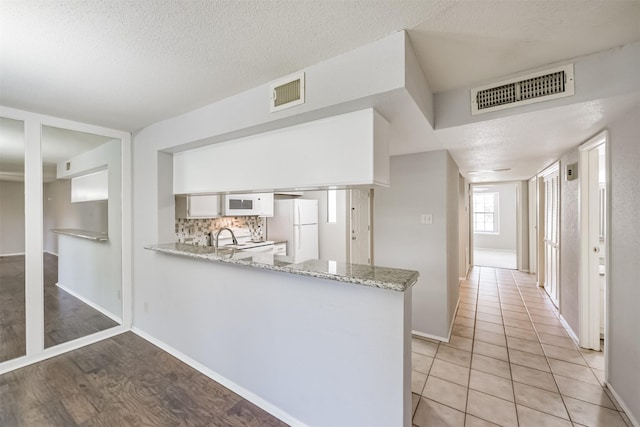 kitchen featuring light stone countertops, tasteful backsplash, kitchen peninsula, white appliances, and white cabinets