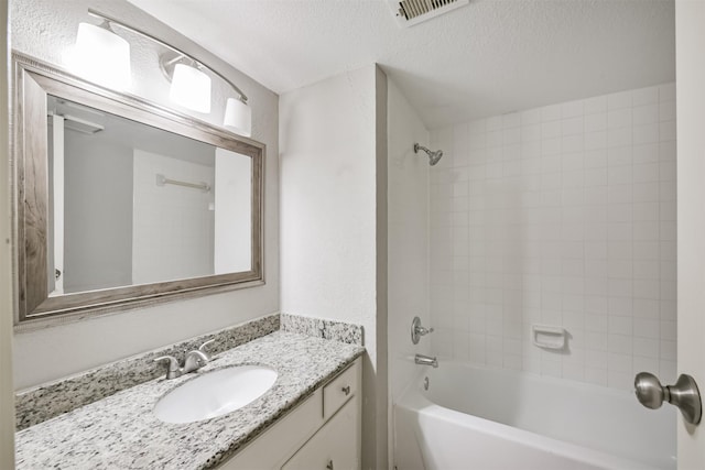 bathroom with vanity, a textured ceiling, and tiled shower / bath