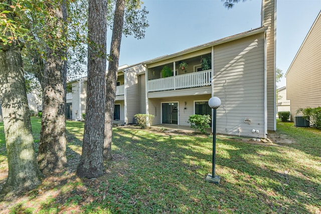 rear view of property with a lawn, a balcony, and central air condition unit