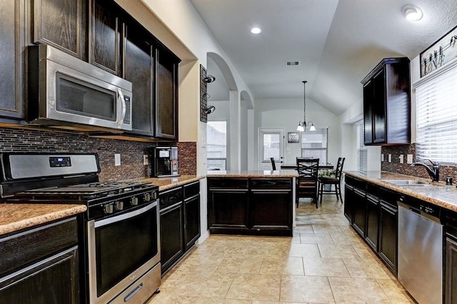 kitchen with pendant lighting, sink, vaulted ceiling, decorative backsplash, and stainless steel appliances