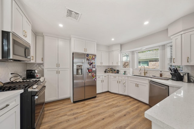 kitchen featuring decorative backsplash, white cabinetry, light hardwood / wood-style flooring, and appliances with stainless steel finishes