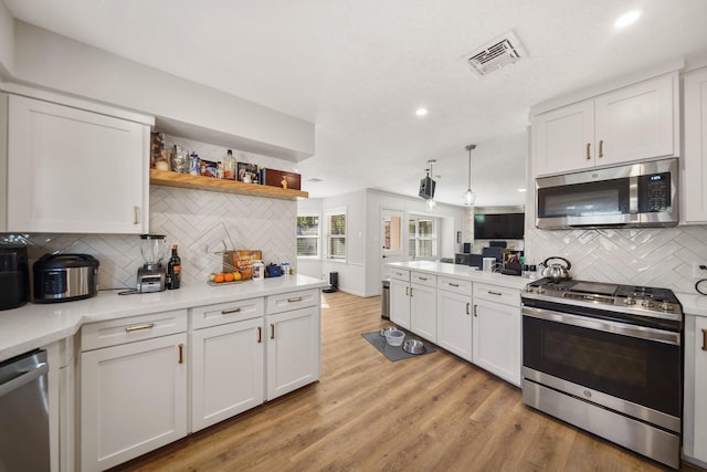 kitchen with backsplash, stainless steel appliances, white cabinetry, and light hardwood / wood-style flooring