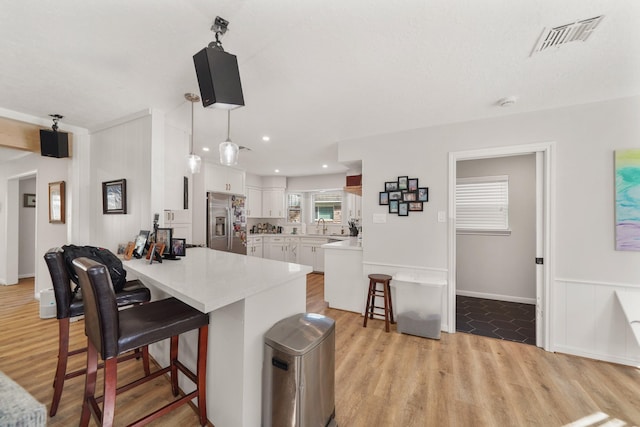 kitchen featuring hanging light fixtures, kitchen peninsula, stainless steel fridge, a kitchen bar, and white cabinets