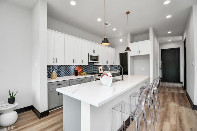 kitchen featuring white cabinetry, hanging light fixtures, a kitchen bar, a kitchen island with sink, and high end stainless steel range