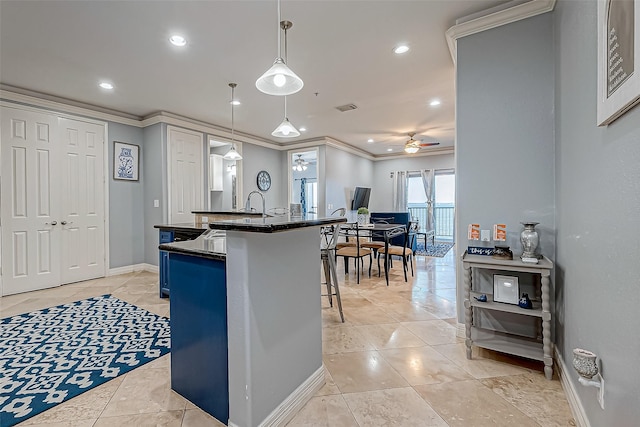 kitchen featuring a breakfast bar, ceiling fan, crown molding, a kitchen island with sink, and decorative light fixtures