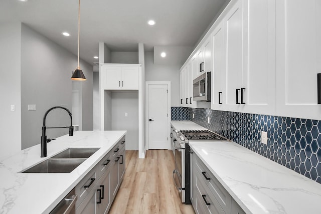 kitchen with sink, hanging light fixtures, light stone counters, white cabinetry, and stainless steel appliances