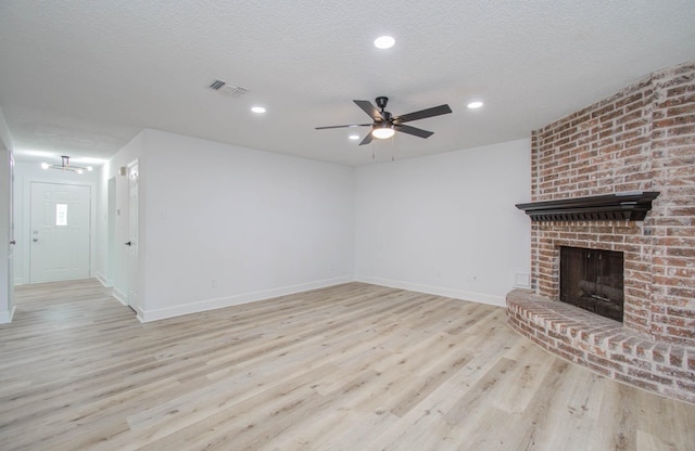 unfurnished living room featuring ceiling fan, light hardwood / wood-style floors, a textured ceiling, and a brick fireplace