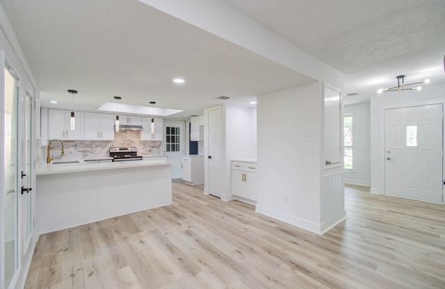 kitchen with kitchen peninsula, stainless steel range with electric stovetop, decorative light fixtures, light hardwood / wood-style flooring, and white cabinets