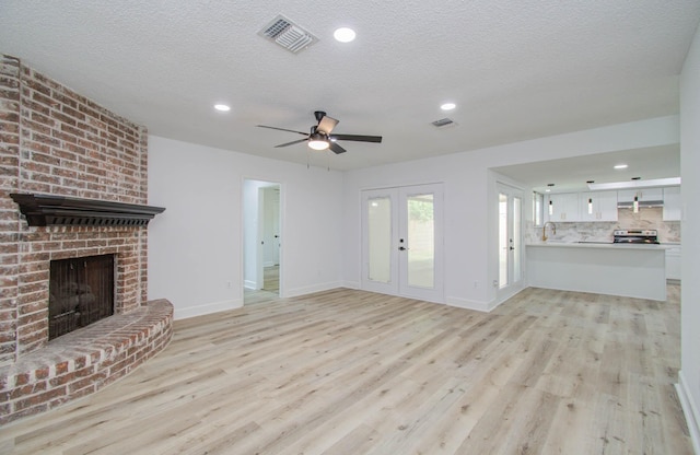 unfurnished living room featuring french doors, a textured ceiling, ceiling fan, a fireplace, and light hardwood / wood-style floors