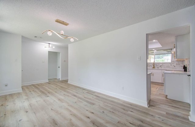 empty room with a textured ceiling, light hardwood / wood-style flooring, and a notable chandelier