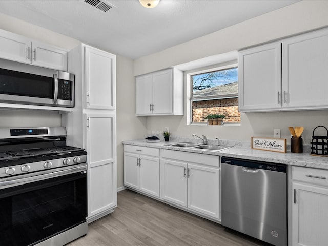 kitchen featuring sink, light stone counters, light hardwood / wood-style floors, white cabinets, and appliances with stainless steel finishes