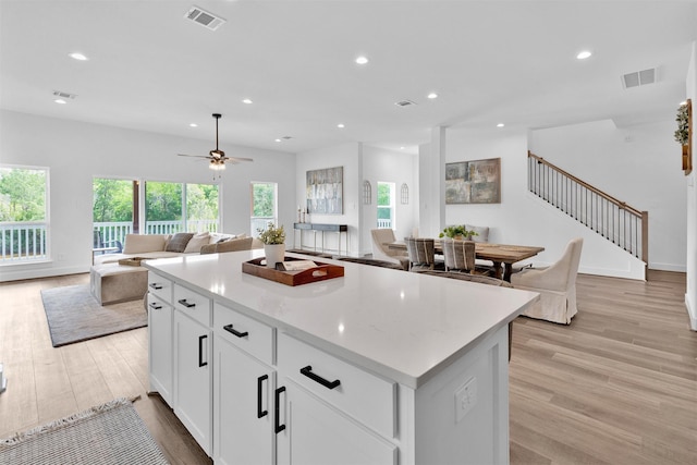 kitchen with a center island, ceiling fan, light wood-type flooring, light stone counters, and white cabinetry