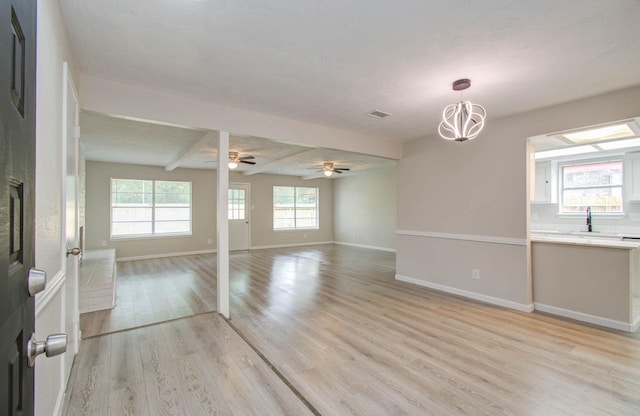 empty room with light wood-type flooring, beam ceiling, and ceiling fan with notable chandelier