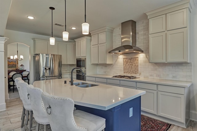 kitchen with appliances with stainless steel finishes, a breakfast bar, wall chimney range hood, and a center island with sink