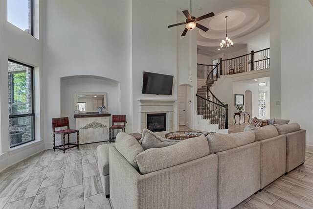 living room with a towering ceiling, a raised ceiling, and ceiling fan with notable chandelier