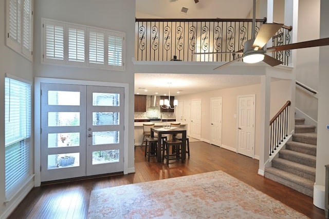 foyer entrance featuring a high ceiling, ceiling fan with notable chandelier, dark hardwood / wood-style floors, and french doors