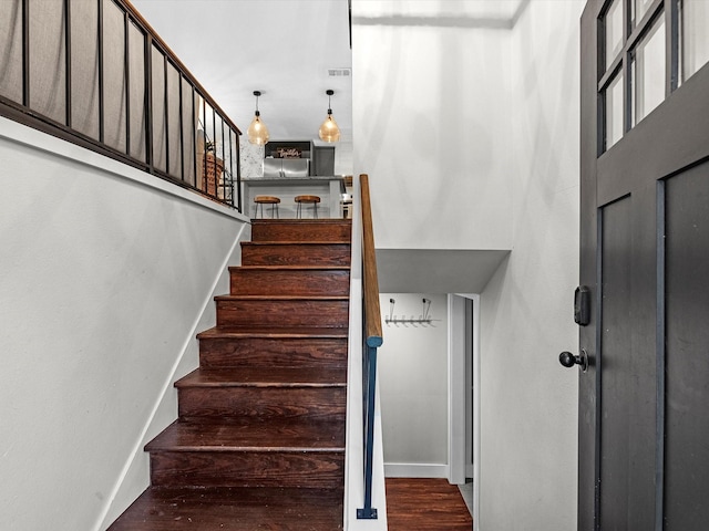 stairway with visible vents, wood finished floors, a towering ceiling, and baseboards