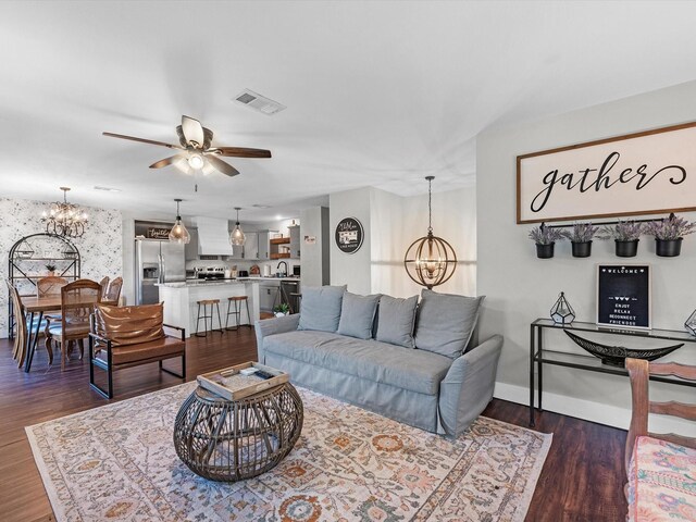 living room featuring ceiling fan with notable chandelier, sink, and dark wood-type flooring