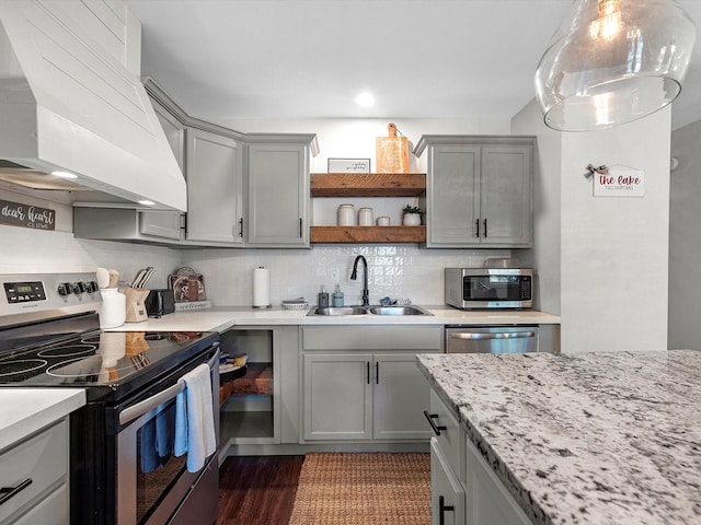 kitchen featuring light stone countertops, appliances with stainless steel finishes, premium range hood, sink, and gray cabinets