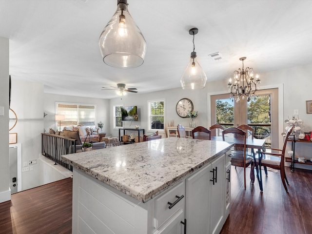 kitchen with light stone counters, white cabinets, dark hardwood / wood-style floors, and ceiling fan with notable chandelier