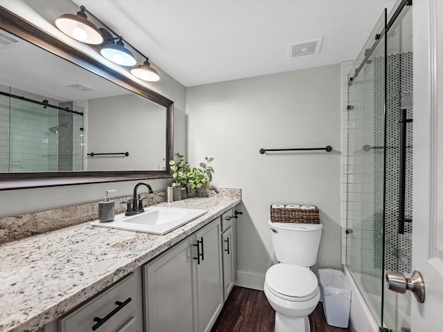 bathroom with visible vents, bath / shower combo with glass door, toilet, wood finished floors, and vanity