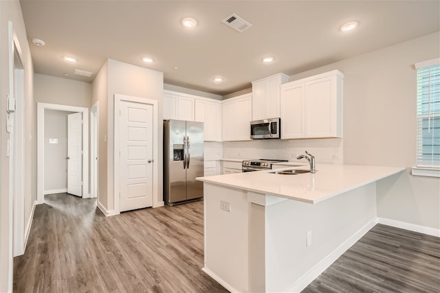 kitchen featuring white cabinetry, sink, stainless steel appliances, kitchen peninsula, and wood-type flooring