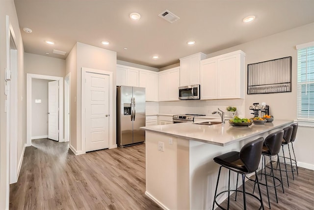 kitchen featuring kitchen peninsula, a kitchen breakfast bar, stainless steel appliances, sink, and white cabinetry