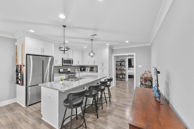 kitchen with a kitchen bar, light stone countertops, stainless steel appliances, white cabinets, and hanging light fixtures