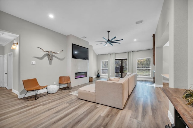 living room with a tiled fireplace, light hardwood / wood-style flooring, and ceiling fan