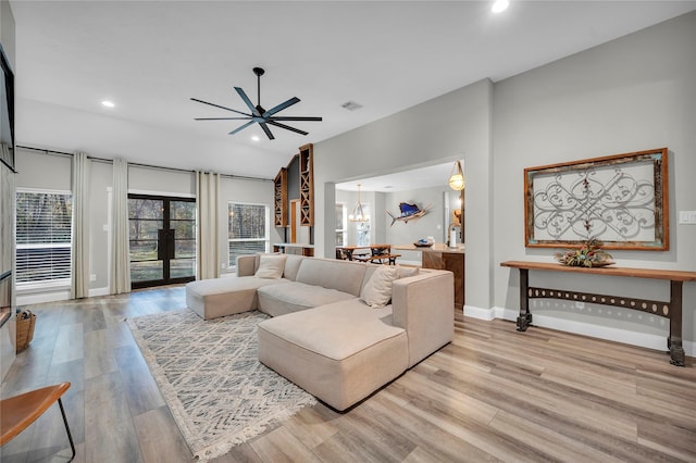 living room with ceiling fan with notable chandelier, light hardwood / wood-style flooring, and french doors