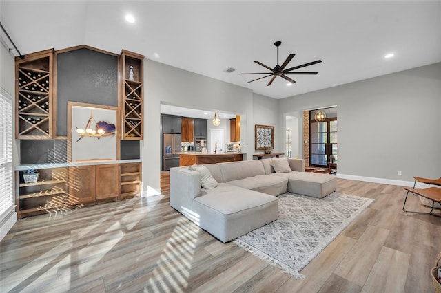 living room with ceiling fan with notable chandelier and light hardwood / wood-style floors