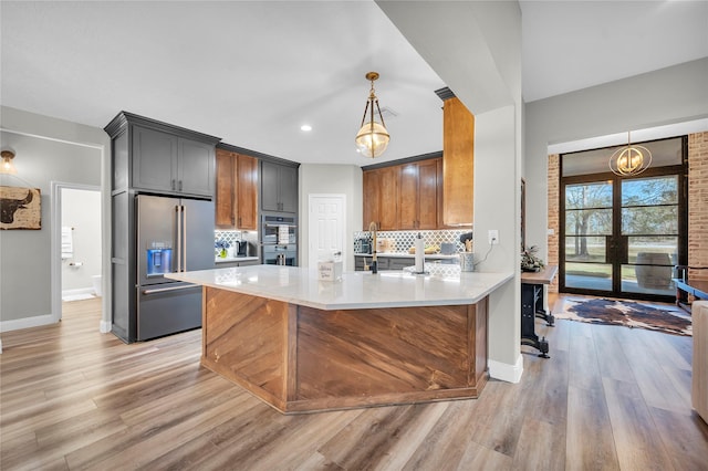 kitchen with pendant lighting, decorative backsplash, light wood-type flooring, high end fridge, and kitchen peninsula