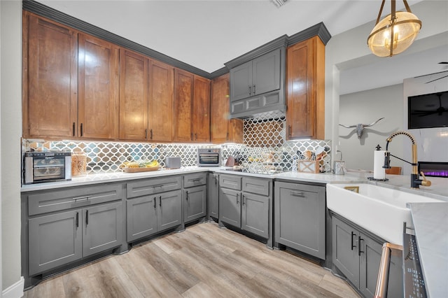 kitchen featuring sink, decorative light fixtures, light wood-type flooring, gray cabinets, and backsplash