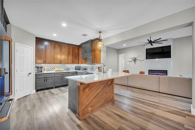 kitchen featuring stainless steel fridge, hanging light fixtures, tasteful backsplash, light stone countertops, and light wood-type flooring