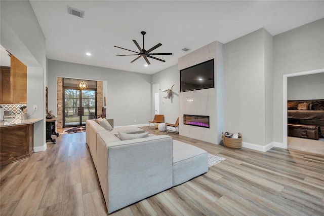 living room with a tile fireplace, ceiling fan, and light wood-type flooring