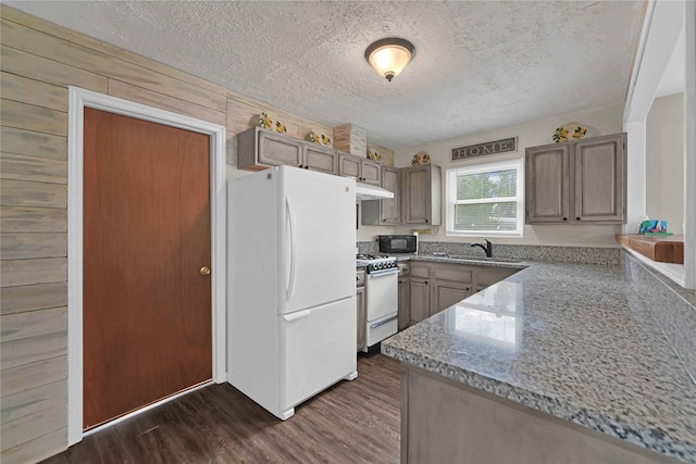 kitchen with white appliances, a textured ceiling, wooden walls, sink, and dark wood-type flooring