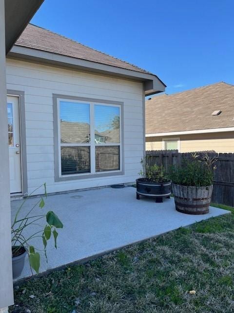 view of side of home with a shingled roof, a patio area, and fence