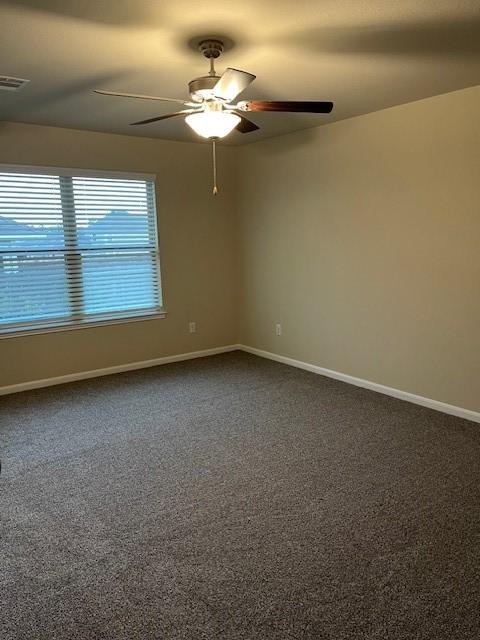 unfurnished room featuring ceiling fan, dark carpet, visible vents, and baseboards